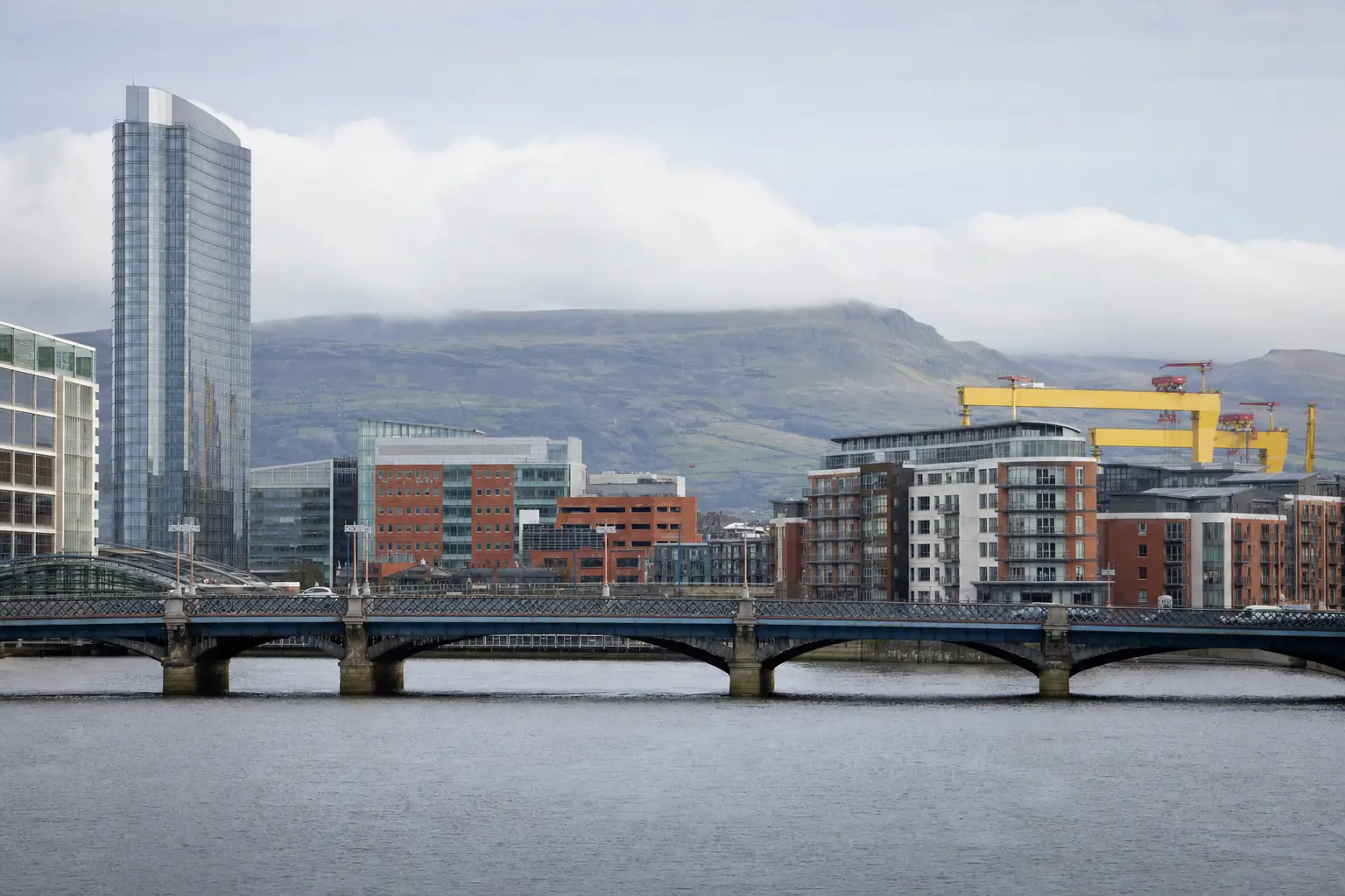 Belfast skyline — the River Lagan, modern city buildings, the Harland & Wolff cranes and the Belfast hills in the distance.